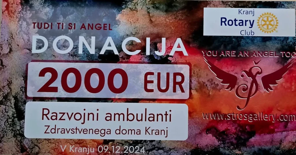 Na barvitem ozadju je prikazan ček z napisom "DONACIJA 2000 EUR Razvojni ambulanti Zdravstvenega doma Kranj", logotip Rotary kluba Kranj in slogan "TUDI TI SI ANGEL / YOU ARE AN ANGEL TOO"